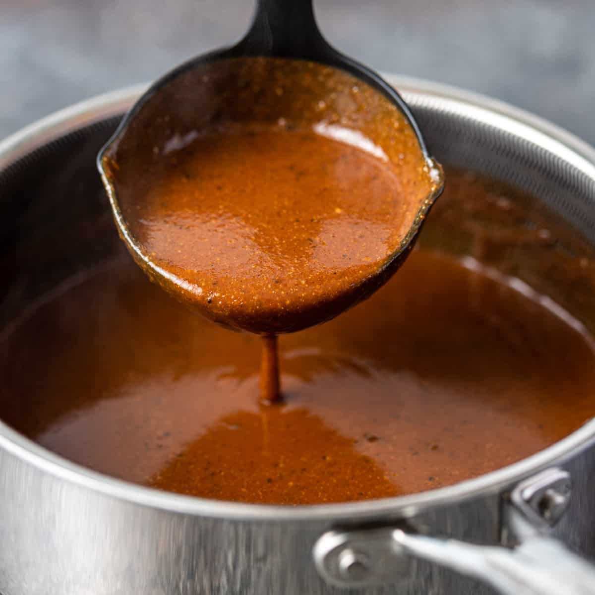 closeup: ladle full of Mexican brown gravy with a bit pouring out into a pot