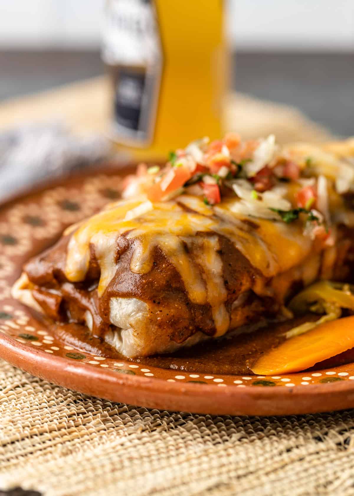 closeup: wet burrito on a ceramic plate with melted cheese and toppings