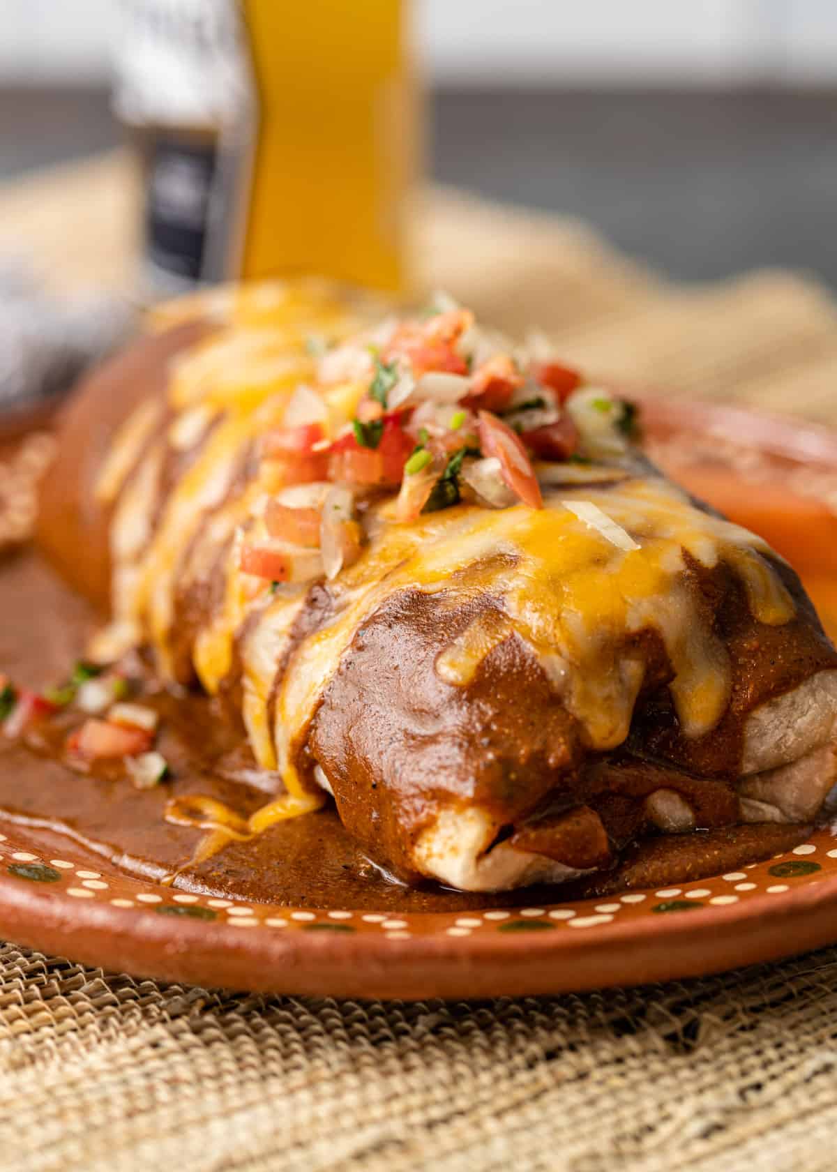 closeup: wet burrito with melted cheese and toppings on a ceramic plate