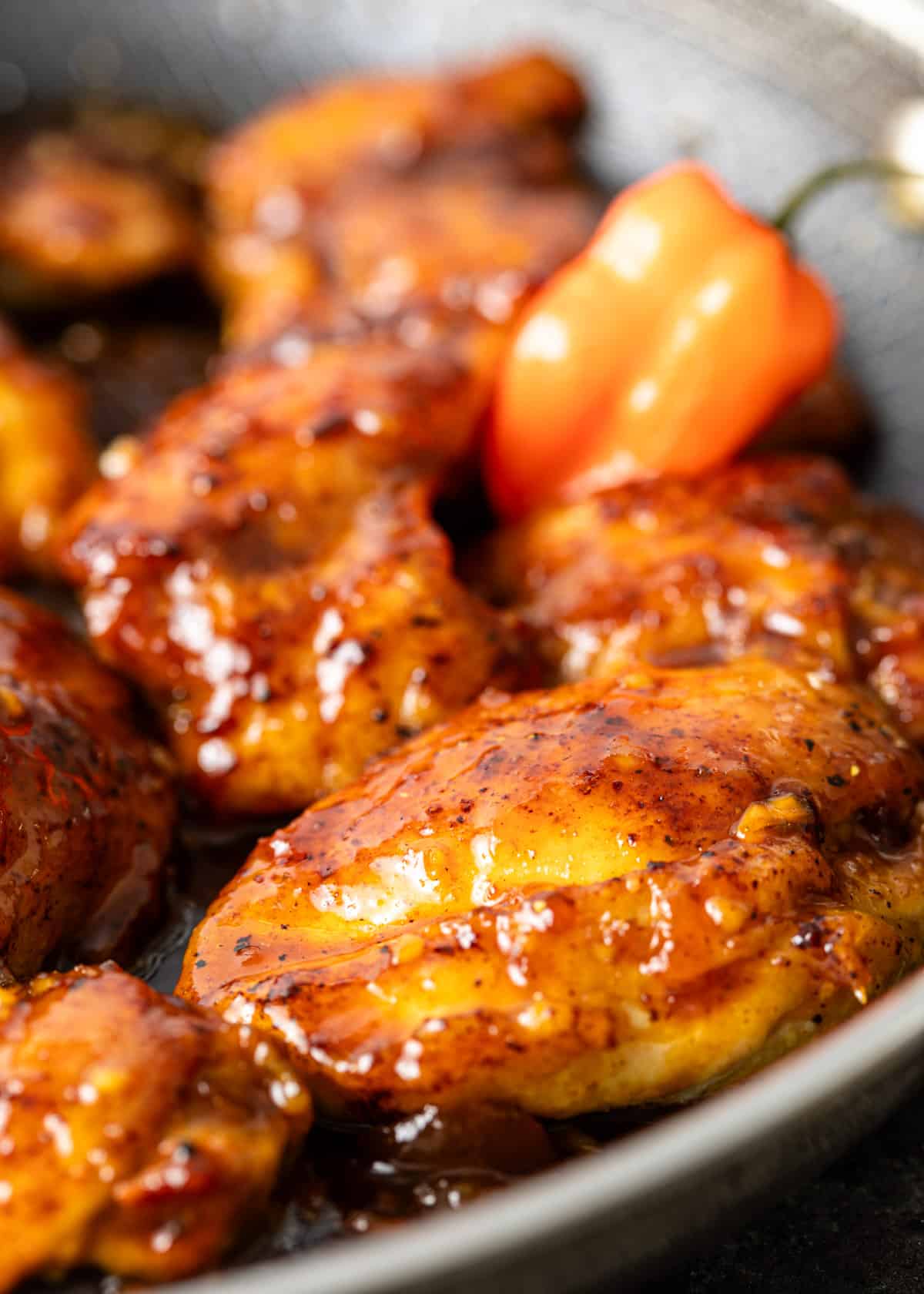 closeup: habanero apricot chicken covered in a sticky sauce in a skillet with a spicy pepper shown