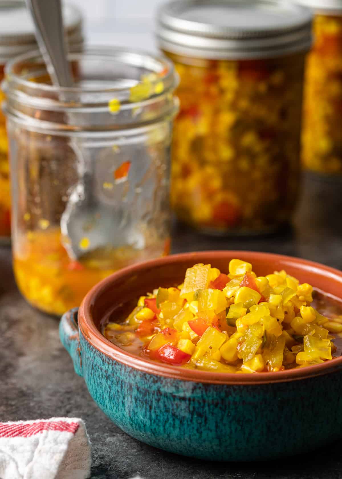 a ceramic bowl of corn relish with a jar visible in the background