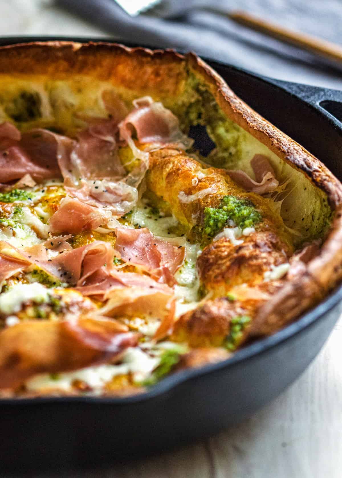 closeup: Dutch baby with pesto and prosciutto in a cast iron skillet