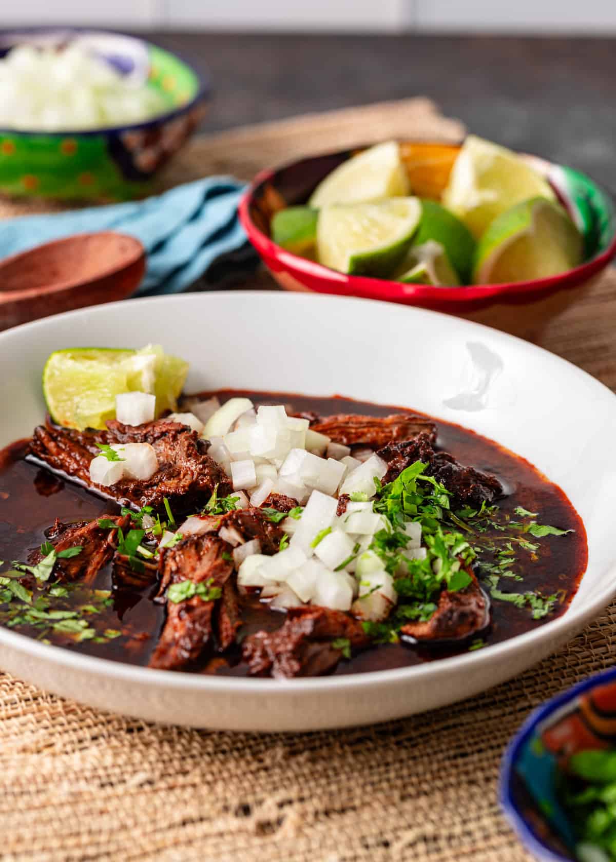 shredded birria in white bowl with onions and cilantro and limes