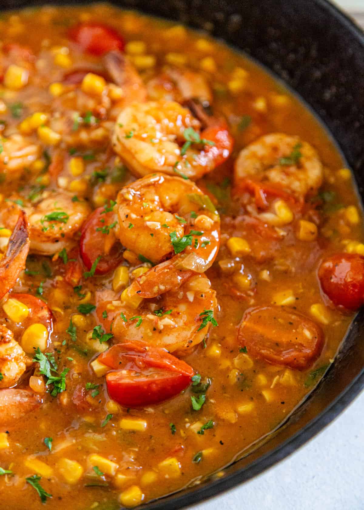 extreme closeup: shrimp and grits recipe cooking in a skillet with shrimp and tomatoes visible