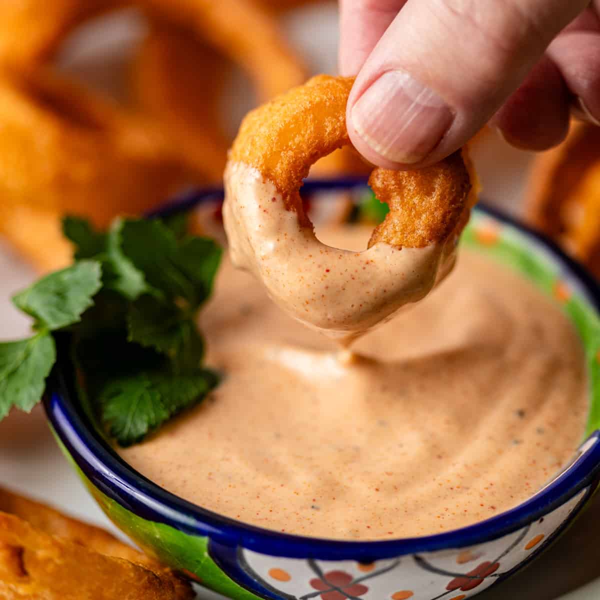 closeup: a hand dipping an onion ring into my comeback sauce recipe
